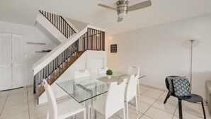 A modern kitchen with a glass dining table, white chairs, a staircase with a black railing, and a ceiling fan. - Waterside Retreat in Fort Lauderdale (Fort Lauderdale)