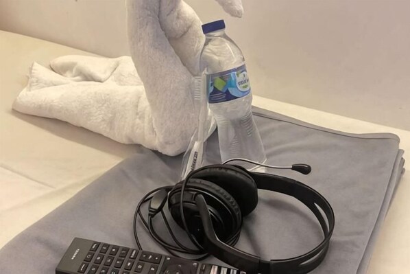A bed with a gray blanket, a bottle of water, headphones, and a remote control. - SHAKTI SLEEP YOGYA (Ngampilan)