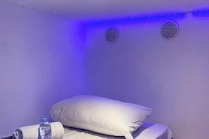 A room with a bed, a pillow, a water bottle, and two air vents on the wall. - SHAKTI SLEEP YOGYA (Ngampilan)