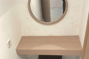 A bathroom with a wooden vanity, a round mirror, and a light switch. - SHAKTI SLEEP YOGYA (Ngampilan)