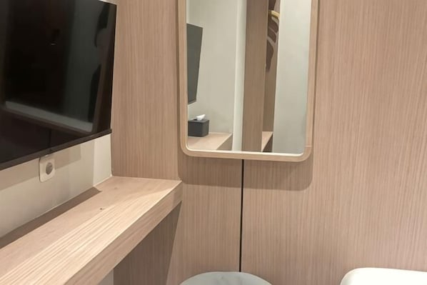A bathroom with a wooden vanity, a mirror, and a toilet. - SHAKTI SLEEP YOGYA (Ngampilan)