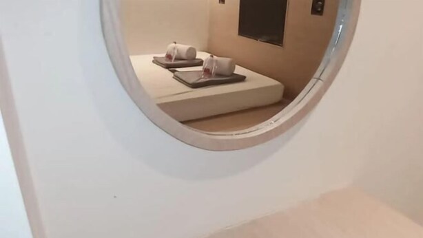 A circular mirror reflecting a room with two beds, a wall-mounted TV, and a small window. - SHAKTI SLEEP YOGYA (Ngampilan)