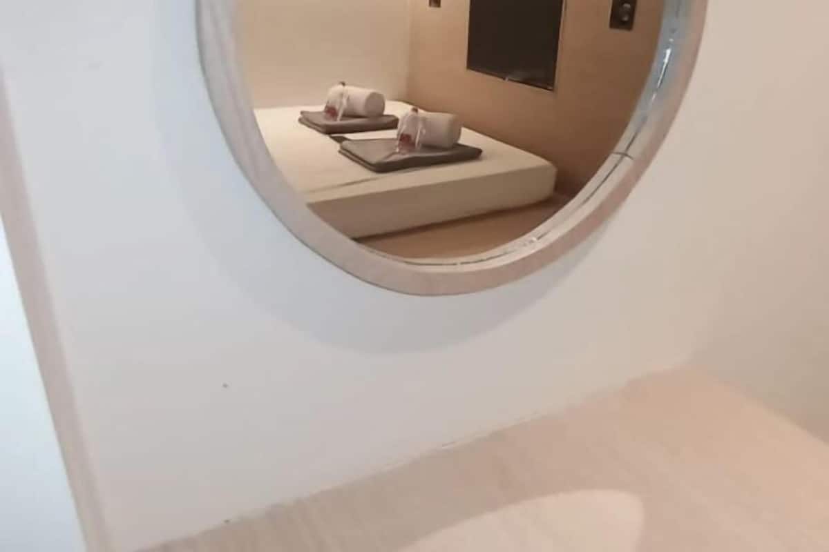 Espejo circular que refleja una habitación con dos camas, un televisor montado en la pared y un ventanal pequeño.