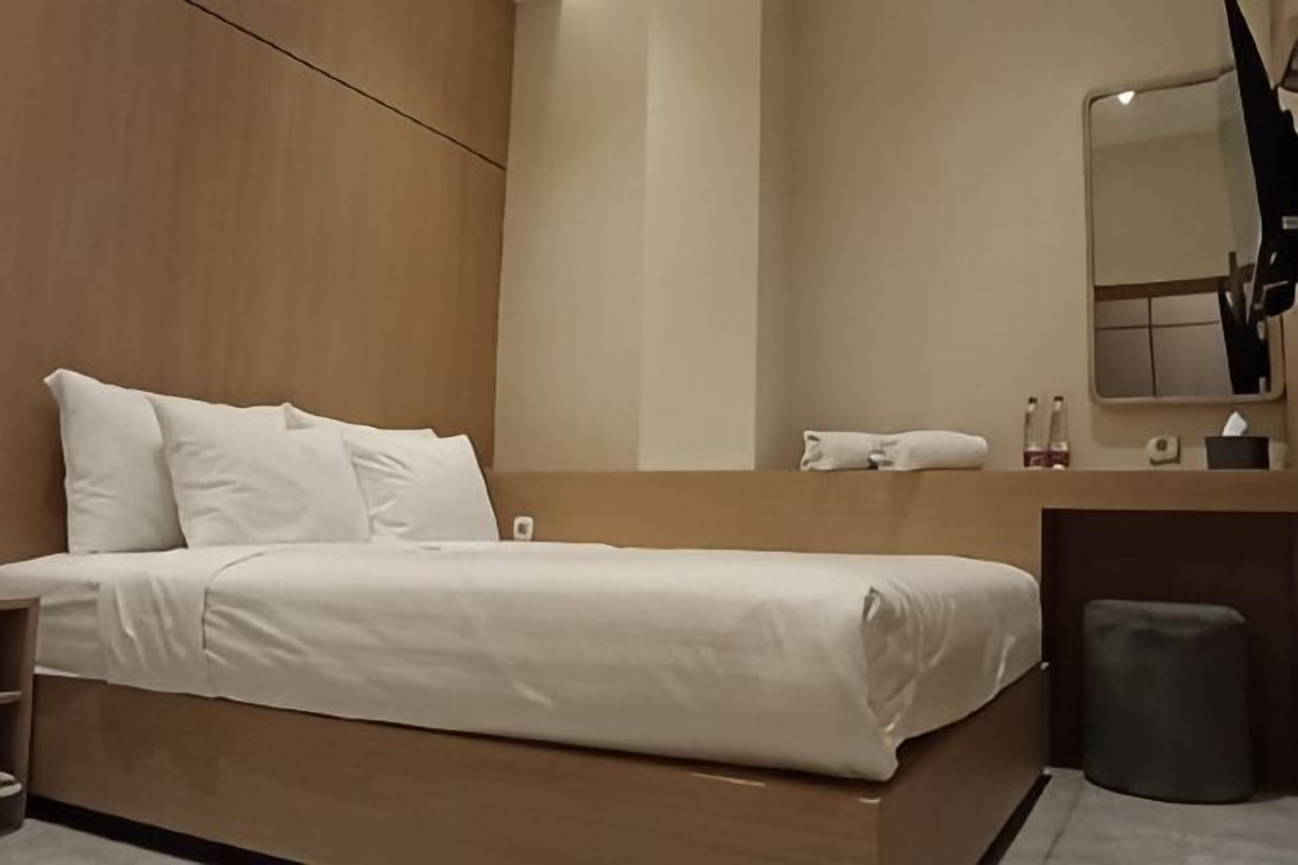A modern hotel room with a bed, a vanity with a mirror, and a small stool.