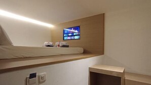 A modern hotel room with a bunk bed, a television mounted on the wall, and a small shelf. - SHAKTI SLEEP YOGYA (Ngampilan)