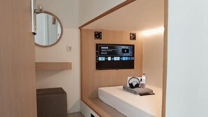 A compact room with a bed, a mounted TV, a mirror, and a small shelf. - SHAKTI SLEEP YOGYA (Ngampilan)