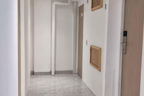 A narrow hallway with a door on the right, a light switch on the wall, and a framed picture. - SHAKTI SLEEP YOGYA (Ngampilan)