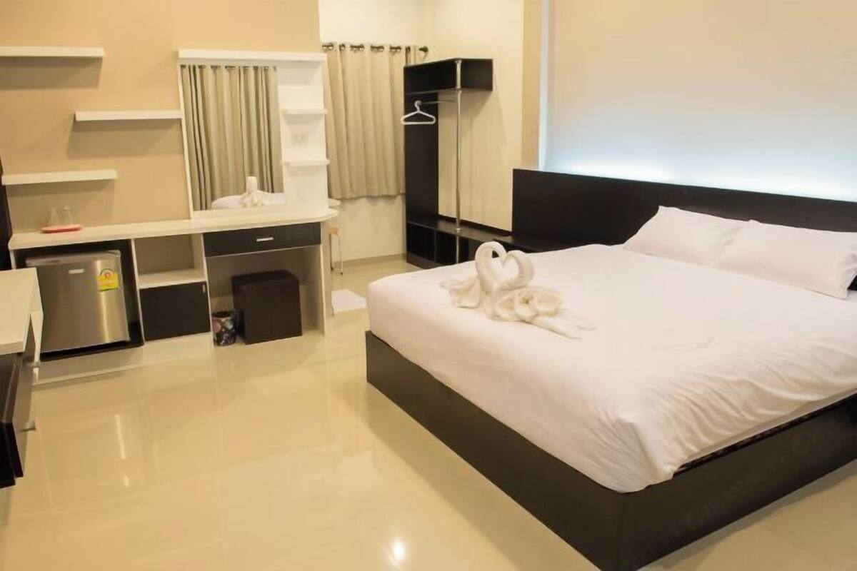 A hotel room with a large bed, a bedside table, a wardrobe, a mirror, and a window with curtains.
