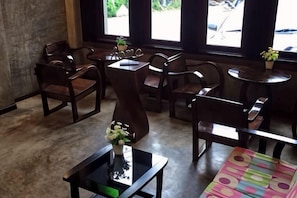 A café interior with wooden furniture, a glass table with a vase, and a view through large windows. - Hug Fang Hotel (Fang)