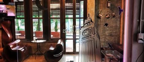 A room with a large window, a chair, a small table, and a decorative item resembling Big Ben.