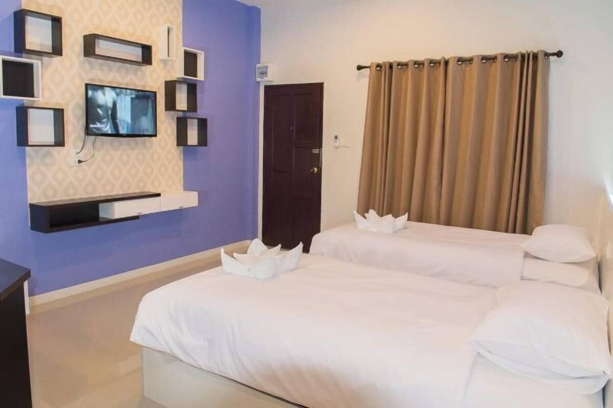A hotel room with two beds, a TV mounted on the wall, and a door.