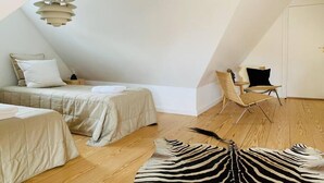 Una habitación con techo inclinado, una cama con cabecera blanca, una silla y un felpudo con estampado de cebra.