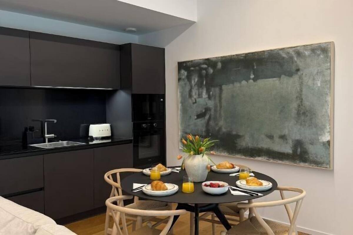 A compact kitchen with dark cabinets, a dining table with chairs, and a large abstract painting on the wall.