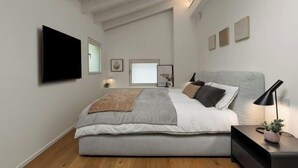 A modern bedroom with a large bed, a flat-screen TV mounted on the wall, and a bedside table with a lamp. - The Golden loft by Aura Luxury Collection (Como)