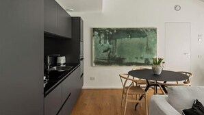 A modern kitchen with dark cabinets, a black countertop, and a round wooden dining table with chairs. A large abstract painting is on the wall above the table. - The Golden loft by Aura Luxury Collection (Como)