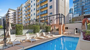 A swimming pool with lounge chairs and a sun terrace, surrounded by modern buildings. - CBD Edge 1BR on Mounts Bay Road (Perth)