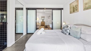 A modern hotel room with a large bed, a bathroom with a glass door, and a living area with a sofa and a lamp. - CBD Edge 1BR on Mounts Bay Road (Perth)