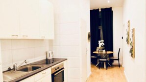 Una cocina compacta con armarios blancos, un lavamanos y una estufa. Hay un comedor con una mesa y sillas.