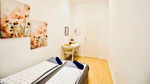 Una habitación con dos camas, una mesita pequeña, una silla, un espejo redondo y una obra de arte floral en la pared.