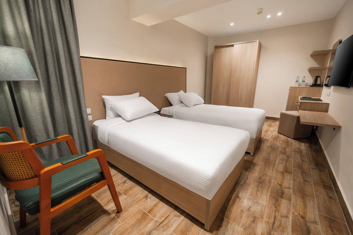Ein Hotelzimmer mit zwei Betten, Holzboden, Schreibtisch mit Stuhl, Fernseher und Kleiderschrank.
