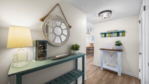 En gang med et trækonsolbord, et dekorativt hjul på væggen, en lampe og en lille hylde med en plante.