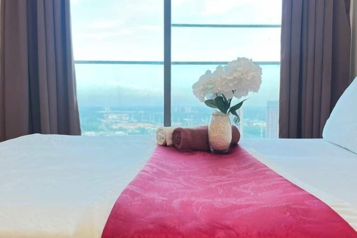A hotel room with a bed, a vase with flowers, and a view of the city.