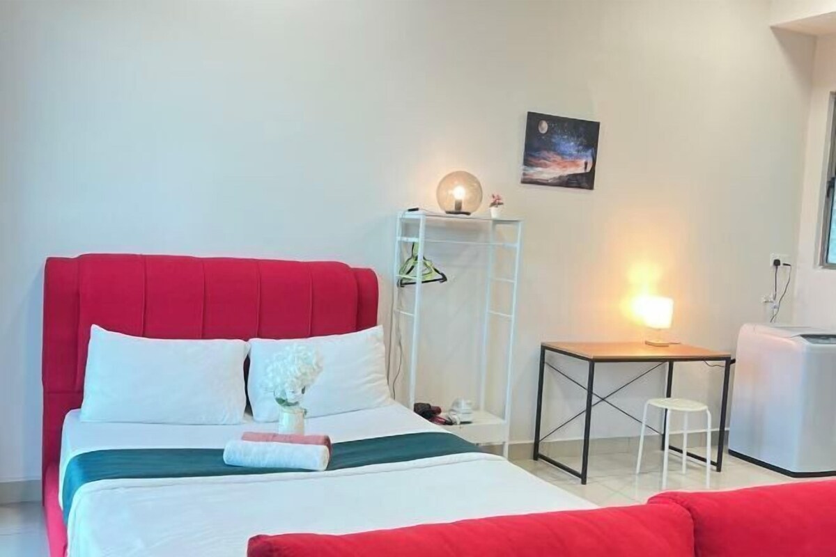 A hotel room with a red bed, white walls, a small table with a lamp, and a night sky painting.