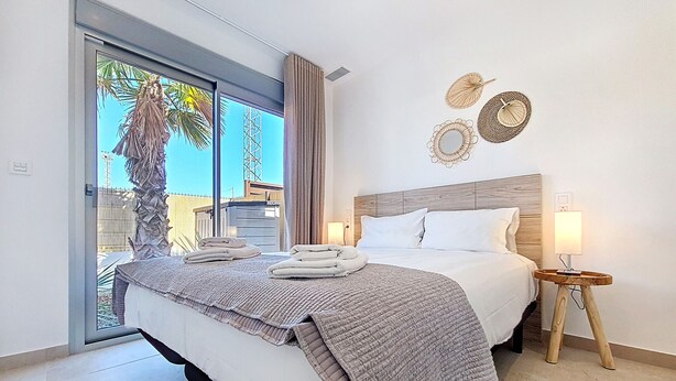 A hotel room with a bed, a bedside table with a lamp, and a view of palm trees through the window. - Villa with private pool, BBQ and large patio (Los Alcazares)