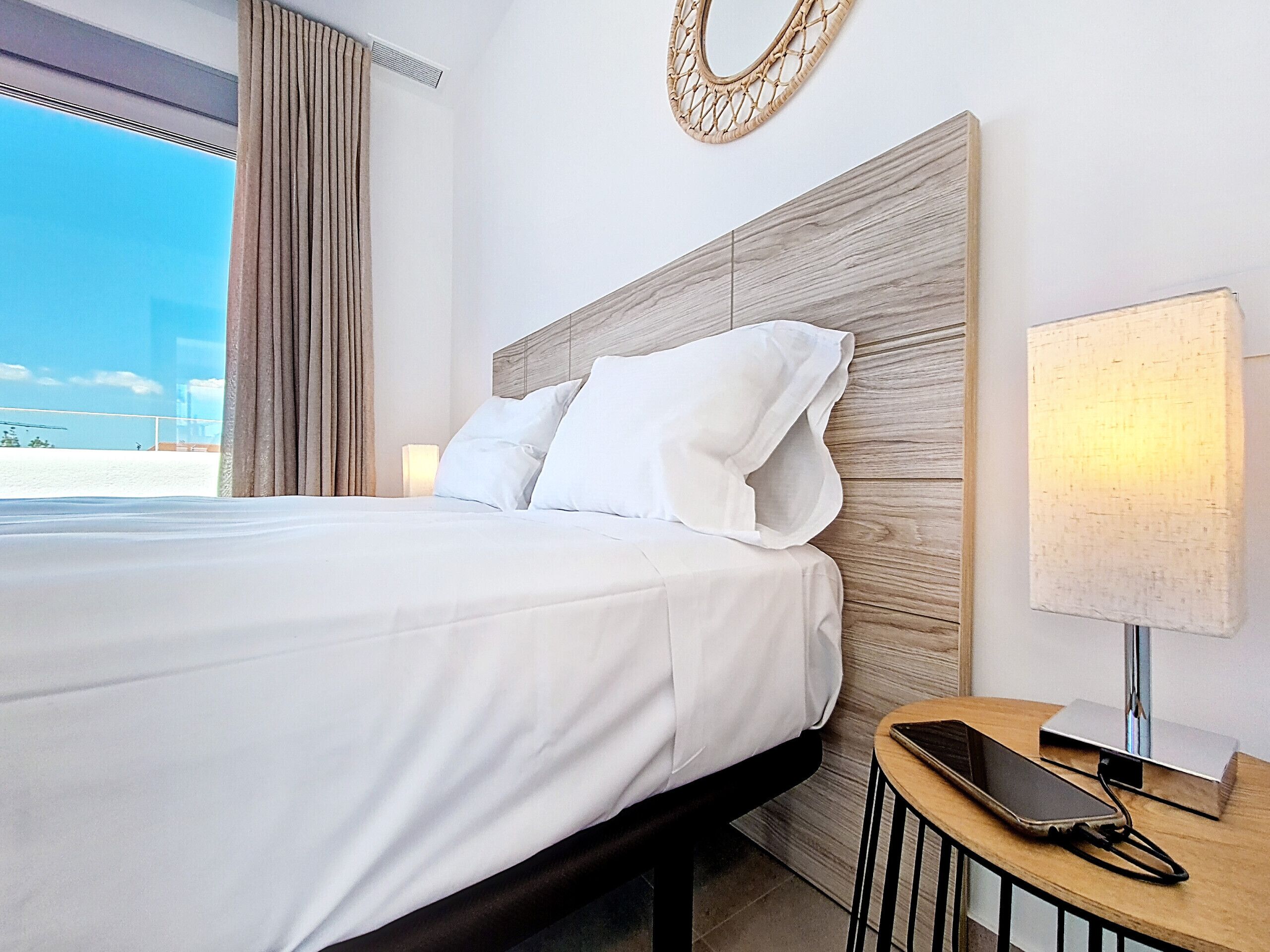 Habitación de hotel con una cama grande, una mesita de noche con lámpara y teléfono, y vista a la playa.
