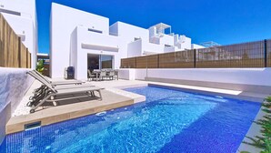 A modern outdoor swimming pool area with a clear blue sky, white buildings, and a covered seating area. - Villa with private pool, BBQ and large patio (Los Alcazares)