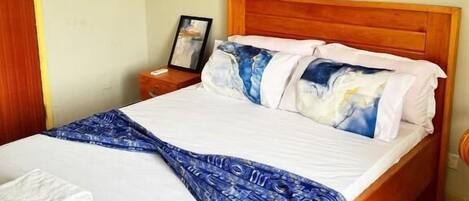 A neatly made bed with a patterned blanket, a wooden headboard, and a painting on the wall.