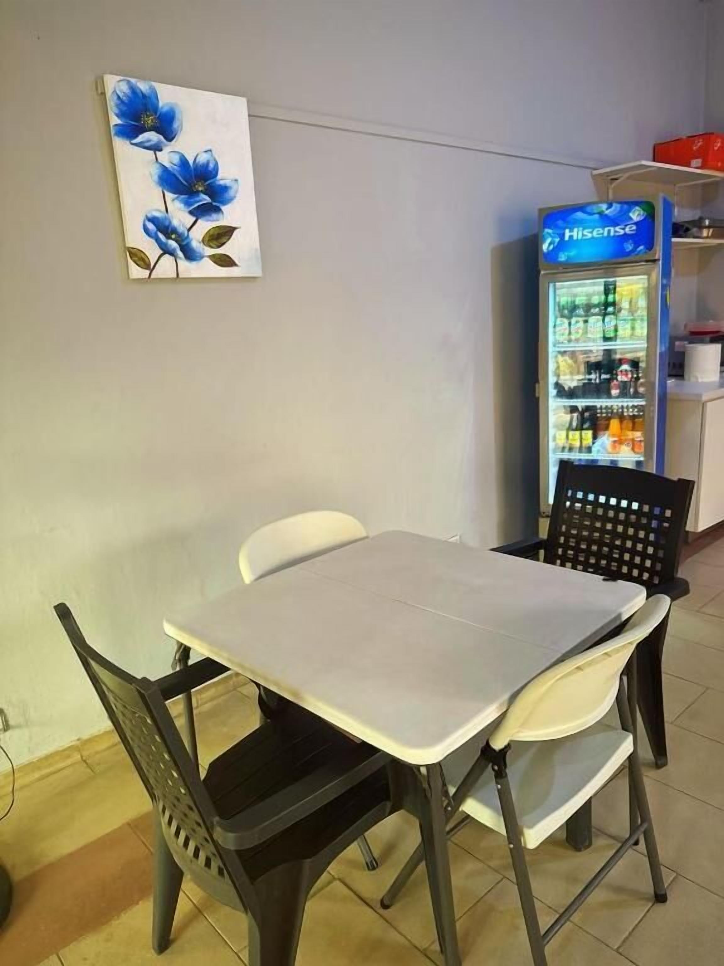 Un comedor con una mesa y sillas, un refrigerador con bebidas, y un cuadro en la pared.