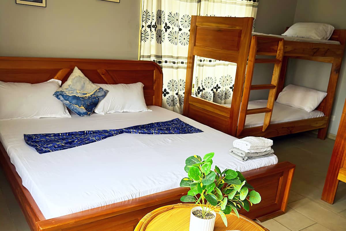Une chambre d’hôtel avec un lit en bois, un lit superposé, une petite table ronde avec une plante et une chaise.