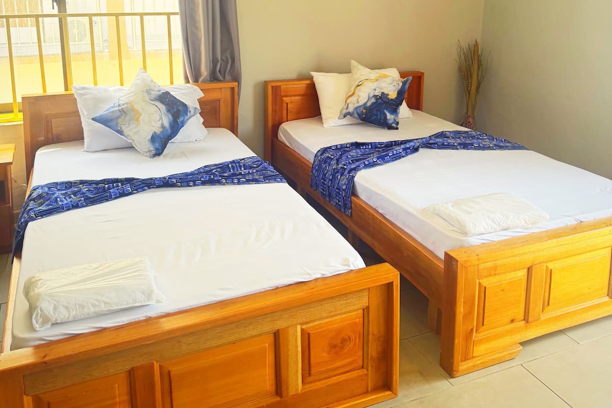 Une chambre d’hôtel avec deux lits en bois, une fenêtre avec des rideaux et deux tableaux encadrés accrochés au mur.