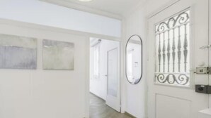 Un couloir doté d’un parquet en point de Hongrie, de murs blancs et d’une porte ornée d’une grille métallique décorative.
