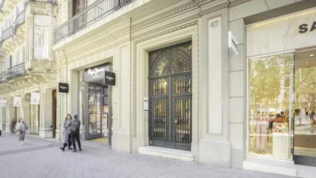 Une façade d’immeuble avec une grande entrée, une boutique sur la gauche et une grande vitrine sur la droite.