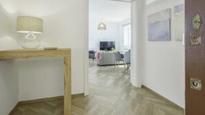Un couloir avec une table en bois et une lampe, qui mène à un espace de vie comprenant un canapé et un téléviseur.