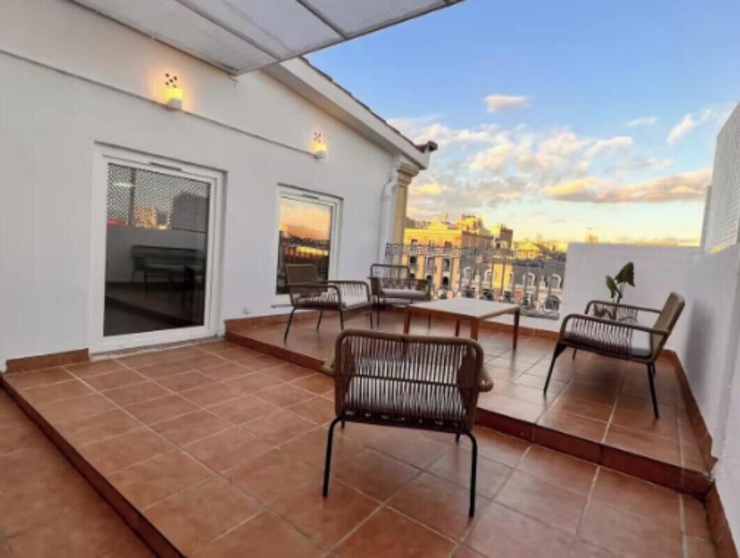 Eine Dachterrasse mit Fliesenboden, zwei Sitzgruppen mit Stühlen und Blick auf die Stadt.