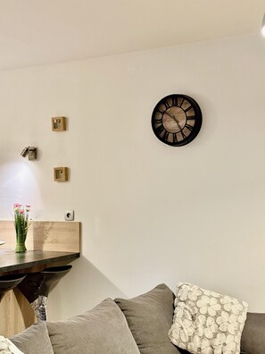 Una sala de estar moderna con una mesa de centro de madera, un sofá con cojines estampados, un reloj en la pared y un pequeño jarrón con flores.