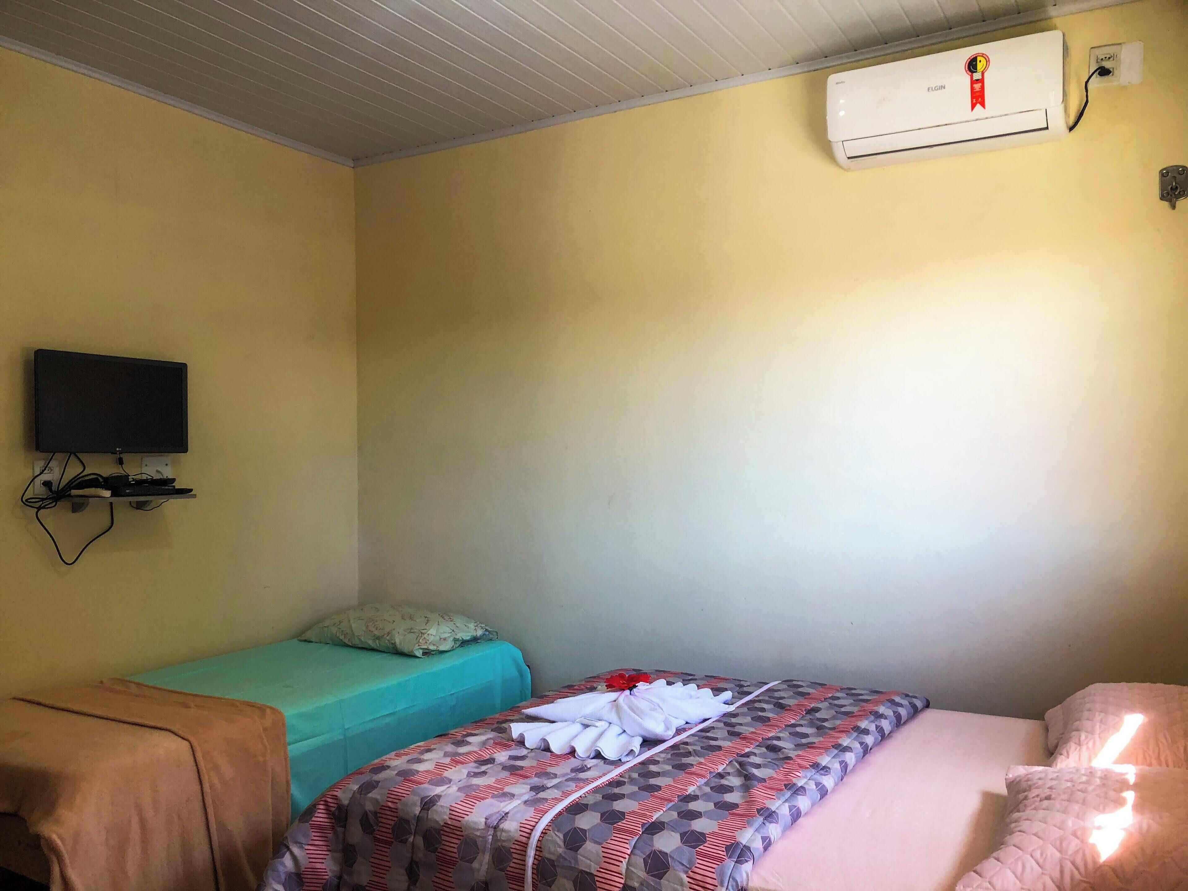 A room with a bed, a TV mounted on the wall, and an air conditioner.