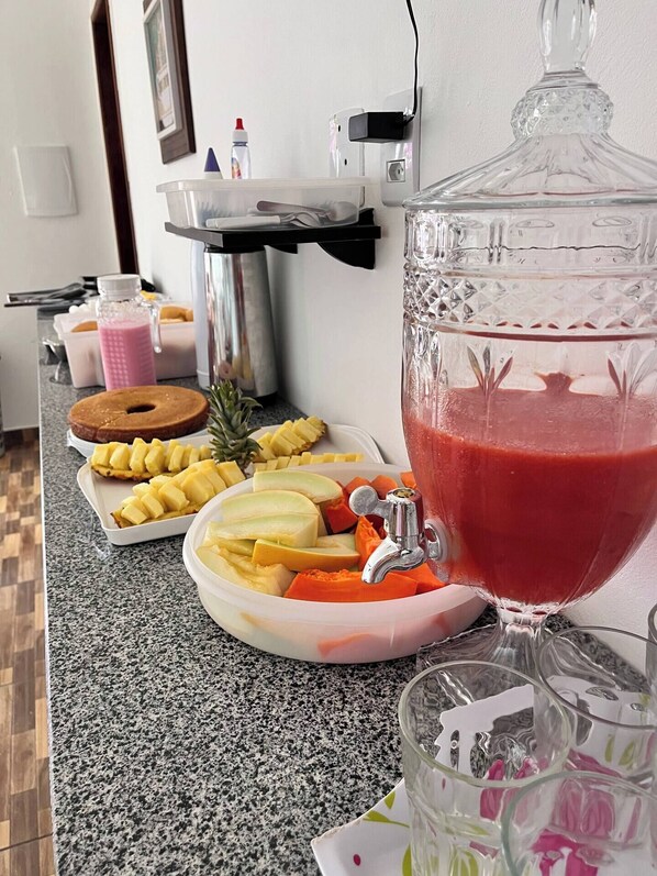 Una encimera de cocina con una bandeja de fruta, una licuadora y un vaso de batido rojo.