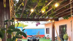 Ein überdachter Patio-Bereich mit Holzterrasse, Reifen-Pflanzgefäßen, einer Hängematte und einem Quad.