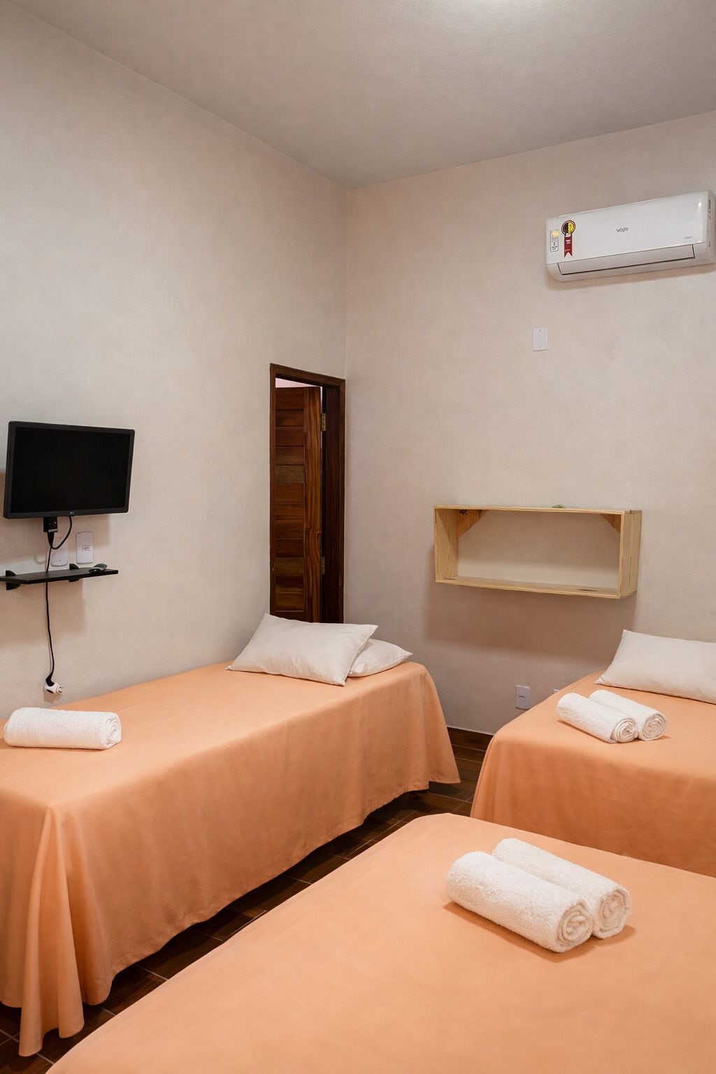 Ein Hotelzimmer mit zwei Betten, einem Fernseher, einer Klimaanlage und einer Holztür.