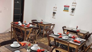 Ein Essbereich mit mehreren Holztischen und Stühlen, an jedem Tisch Teller, Tassen und orangefarbene Servietten.