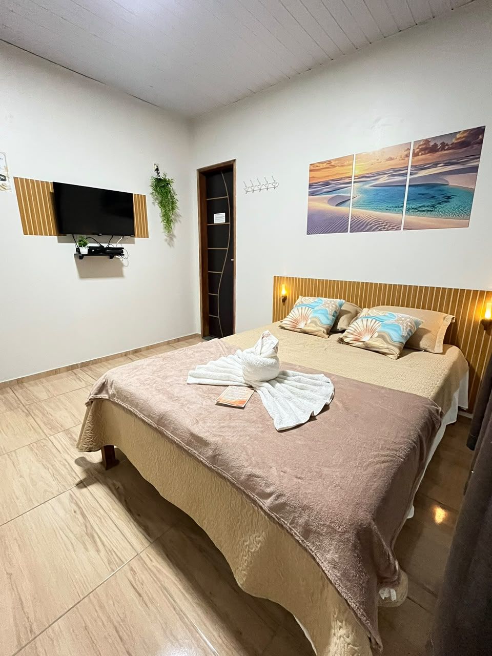 Camera d'albergo con un letto, una TV a schermo piatto fissata al muro, un quadro sopra il letto e una porta che conduce a un'altra stanza.