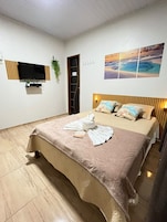 Habitación de hotel con cama, televisor de pantalla plana montado en la pared, un cuadro sobre la cama y una puerta que da a otra habitación.
