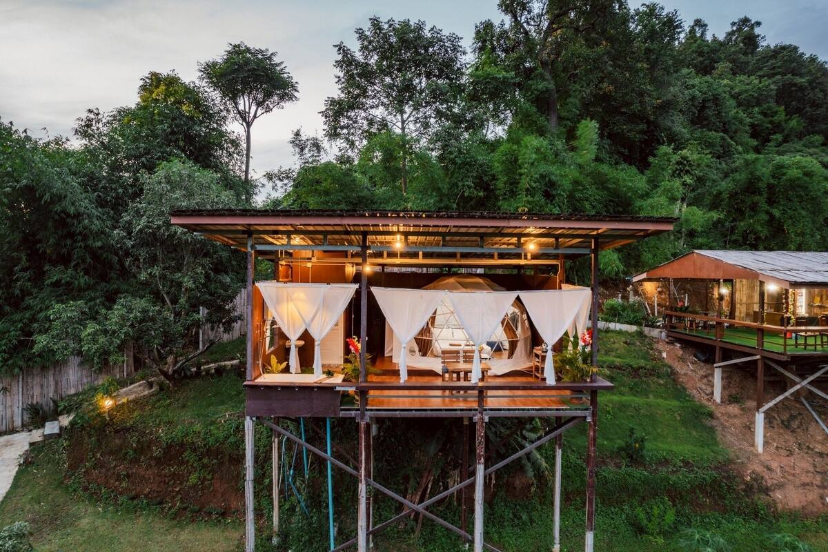 A treehouse with a wooden deck and a covered seating area.