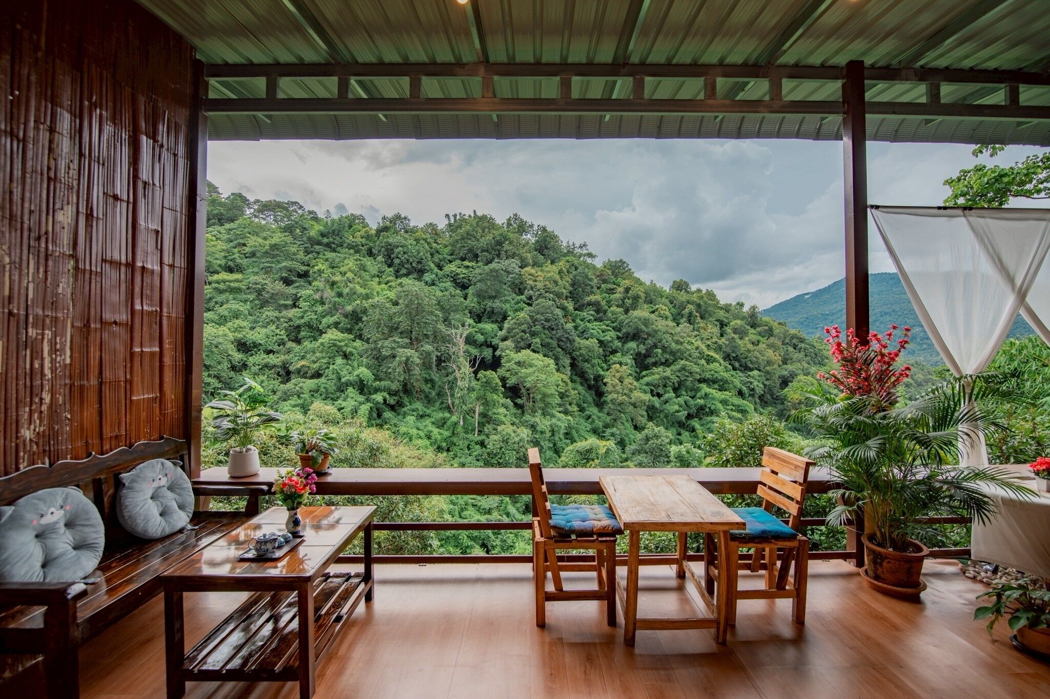 A wooden deck with a table and chairs, overlooking a lush forested hillside.