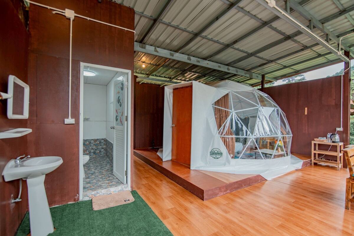 A room with a wooden floor, a white sink, a door leading to a bathroom, and a tent-like structure with a logo.