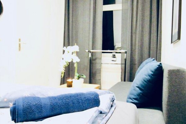 A hotel room with a bed, a nightstand, a lamp, a window with curtains, and a wall-mounted TV.